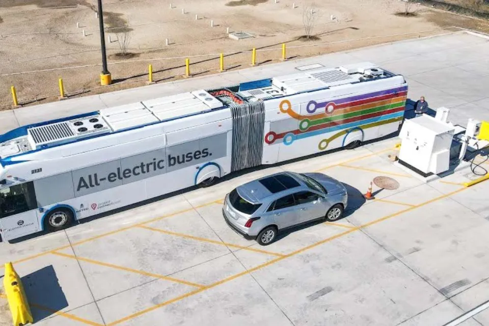 Aerial view of electric bus parked next to silver SUV in parking lot in Austin, Texas. Bus says "All eelctric buses" on side.